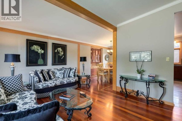 Living room with floral sofas, glass coffee table, hardwood floors, and an adjacent dining area. - 5108 Brockington Road Nw, Calgary