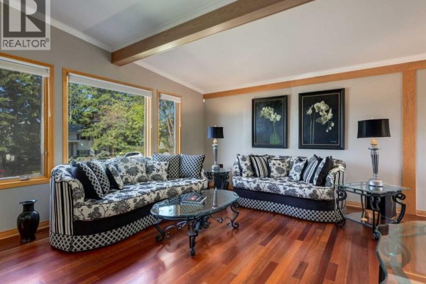Living room with two sofas, glass coffee tables, hardwood floors, and large windows with tree views. - 5108 Brockington Road Nw, Calgary