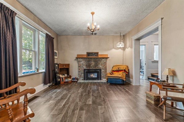 Living room with a brick fireplace, wood flooring, a chandelier, and two chairs. - 51098 Yale Road, Rosedale, Rosedale
