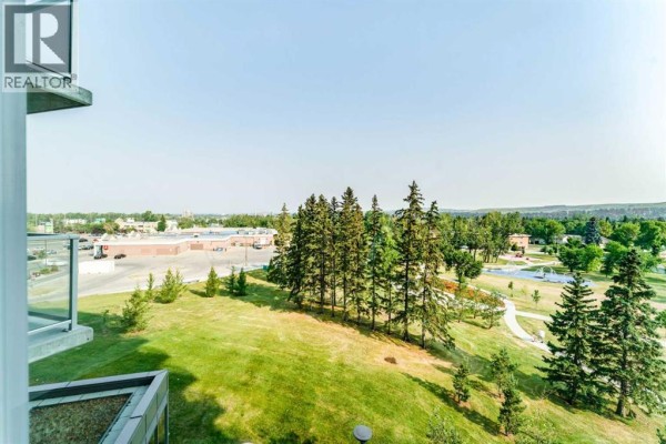 Open concept living space with white sofa, kitchen area, and view of hallway with doors. - 511, 30 Brentwood Common Nw, Calgary
