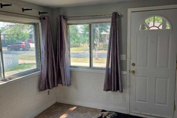 View of a room with white brick walls, large windows, grey curtains, and a white front door. - 511 12c Street N, Lethbridge