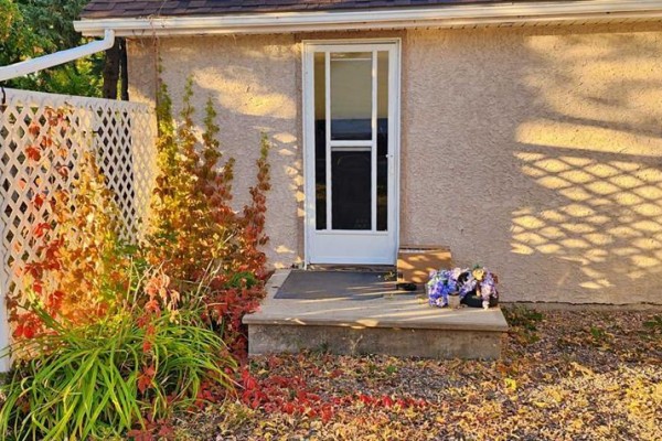 Close-up of a front door with a screen door and a concrete stoop with a welcome mat and artificial flowers. - 5111 53 Street, Mannville