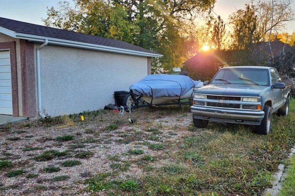 Side view of a garage with a covered boat on a trailer and a dark blue pickup truck parked beside it. - 5111 53 Street, Mannville