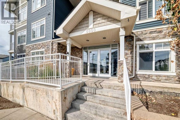 Close-up of the apartment building's main entrance with stairs, railings, and double glass doors. - 5114, 155 Skyview Ranch Way Ne, Calgary