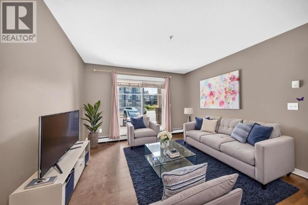 Living room with a gray sofa, armchairs, a glass coffee table, and a television on a white stand. - 5114, 155 Skyview Ranch Way Ne, Calgary