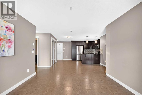 Open-concept living area with hardwood floors, leading to a modern kitchen with dark cabinets and stainless steel appliances. - 5114, 155 Skyview Ranch Way Ne, Calgary