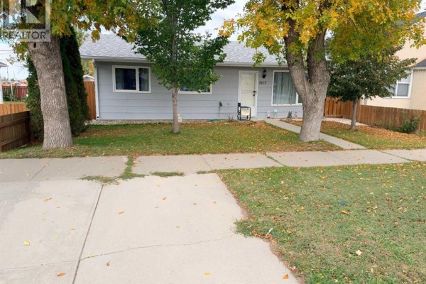 View of the front exterior from the sidewalk, showing the house, lawn, and trees. - 5117 45 Avenue, Taber