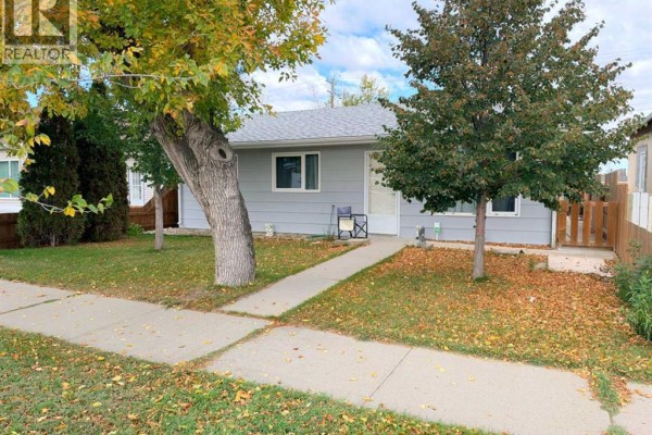 Side view of the light grey bungalow with trees and fallen leaves in the yard. - 5117 45 Avenue, Taber