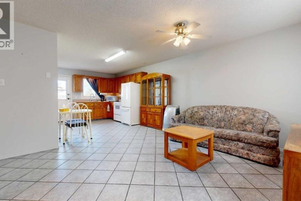Open concept living area and kitchen with tiled floors, floral sofa, and wooden cabinets. - 5117 45 Avenue, Taber