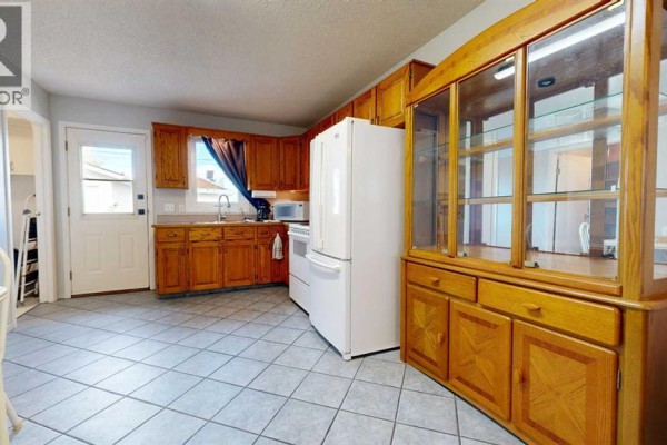 Kitchen area with wood cabinets, white appliances, tiled floor, and a large glass-front cabinet. - 5117 45 Avenue, Taber