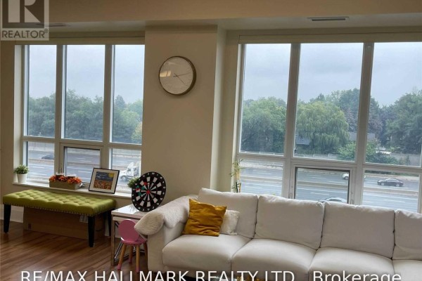 A living room featuring a white sectional sofa, large windows, and city views. - 512 - 100 Harrison Garden Boulevard, Toronto