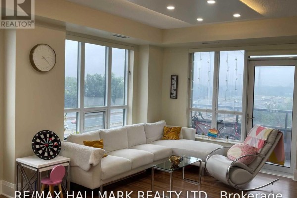 A living room with a white sectional, glass coffee table, and a balcony door. - 512 - 100 Harrison Garden Boulevard, Toronto