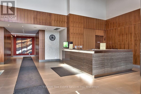 Reception desk area in the condominium lobby with wood paneling and modern lighting. - 512 - 1055 Southdown Road, Mississauga