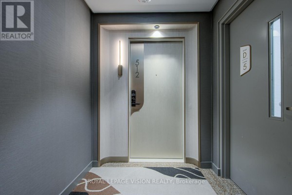 Apartment entrance door labeled 512, with wood-look textured walls and a decorative wall sconce. - 512 - 155 Merchants' Wharf, Toronto