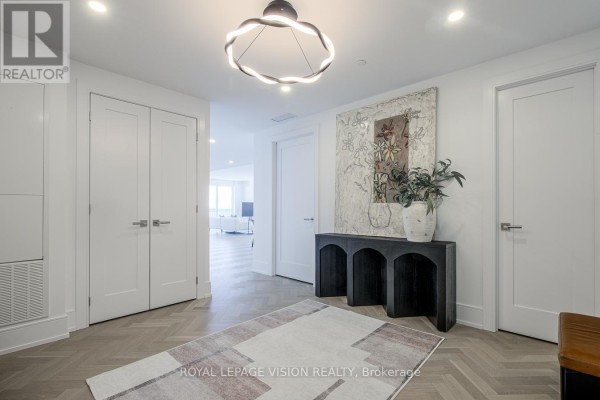 Wide apartment foyer with herringbone wood floors, white doors, and a console table with artwork. - 512 - 155 Merchants' Wharf, Toronto