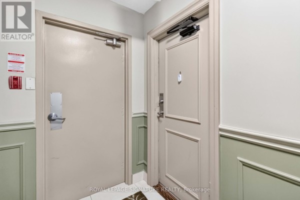 Hallway showing two neutral-colored doors, one with a fire alarm and extinguisher mounted nearby. - 512 - 1615 Bloor Street, Mississauga