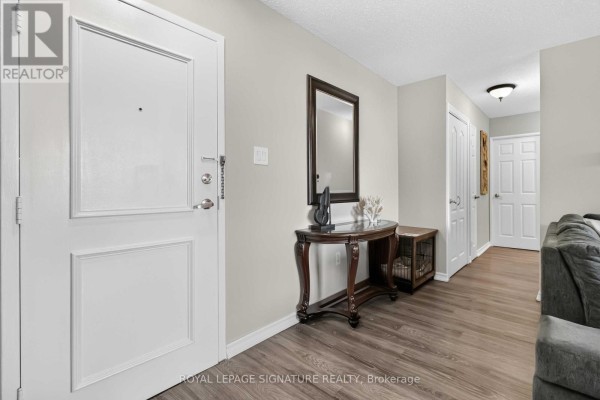 Entryway with a white door, dark wood console table with mirror, and grey wood-look flooring. - 512 - 1615 Bloor Street, Mississauga