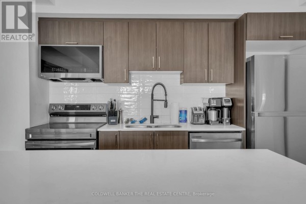 Kitchen bar with four black stools, adjacent to stainless steel appliances and wooden cabinetry. - 512 - 5 Chef Lane, Barrie