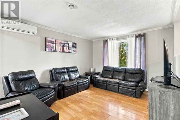 A living room with light grey walls, black leather couches, a TV, and wood floors. - 512 Main Road, St John S