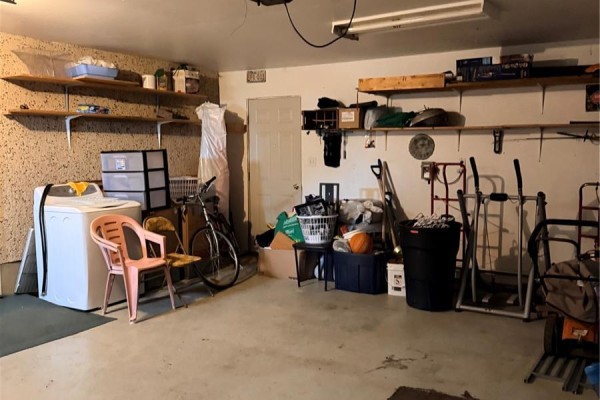 Garage interior with laundry machines, bicycles, storage shelves, and various household items. - 512 Mcnab Street, Burstall