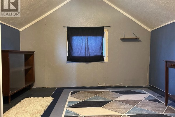 Room with geometric rug, dark window covering, and wooden cabinet. - 512 Railway Avenue, Lampman
