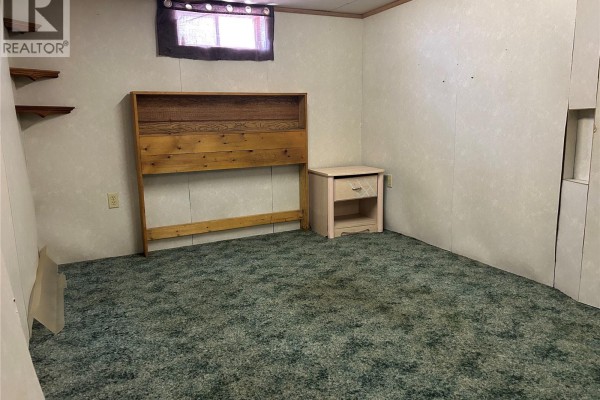 Bedroom with green carpet, wooden headboard, and pink nightstand. - 512 Railway Avenue, Lampman