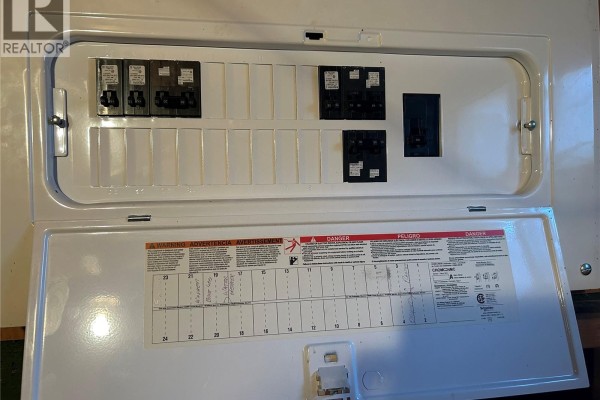 Open electrical panel with circuit breakers and warning labels. - 512 Railway Avenue, Lampman