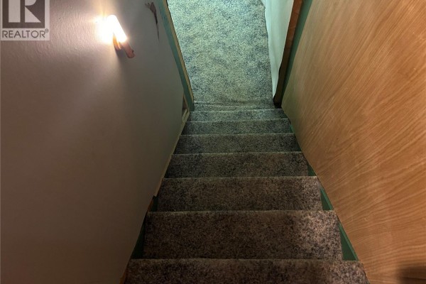 Carpeted stairs descending between pale green and wood-paneled walls. - 512 Railway Avenue, Lampman