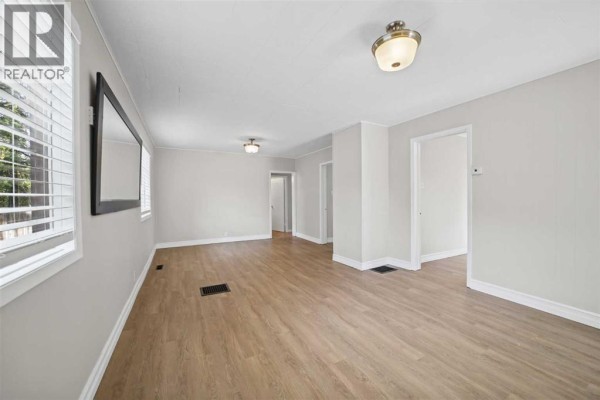 Living room with light wood laminate flooring, pale gray walls, and large windows. - 5122 49 Street, Olds