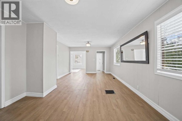Living room with light wood laminate flooring, pale gray walls, and a large mirror. - 5122 49 Street, Olds