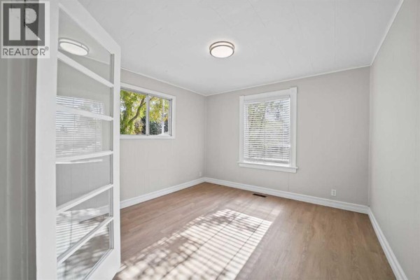 Bedroom with light wood laminate flooring, pale gray walls, and double glass doors. - 5122 49 Street, Olds