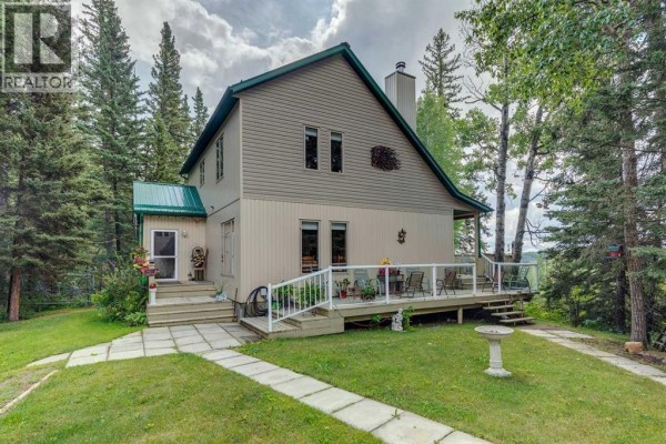 View of the beige house from the side, showing a large deck with glass railings. - 5123 Township Road 342 A, Rural Mountain View County
