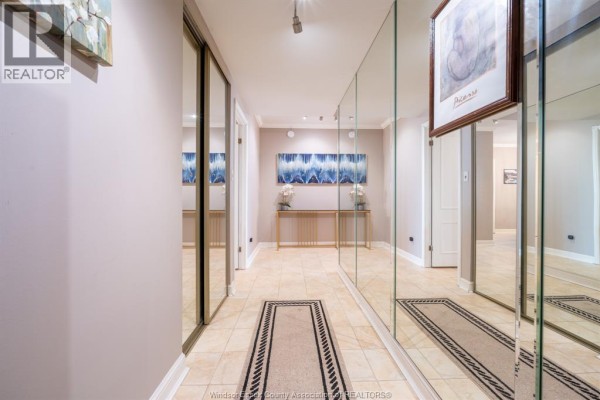 Hallway with tiled floors, mirrored walls, and artwork leading to apartment doors. - 5125 Riverside Drive East Unit# 204, Windsor