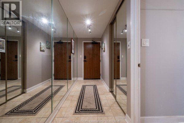 Hallway with tiled floors, mirrored walls, and wood doors leading further into the building. - 5125 Riverside Drive East Unit# 204, Windsor