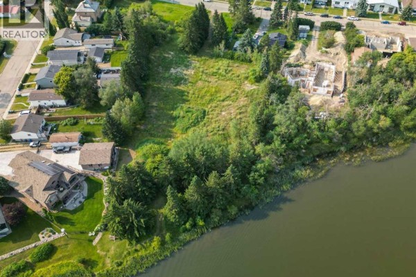 Overhead view of a vacant lot with trees and some house foundations, adjacent to a lake and existing homes. - 5128 & 5124 56 Street, Innisfail