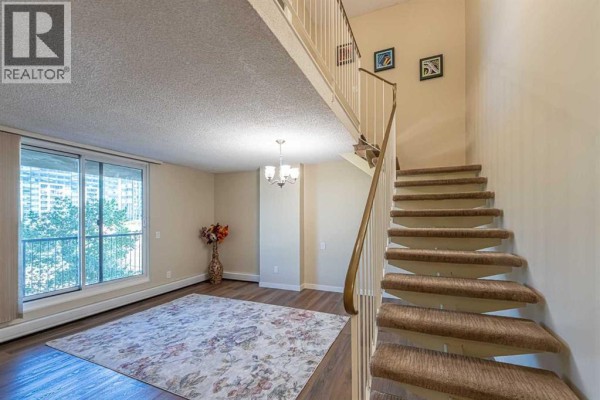 A living room with a large area rug, sliding glass doors, and a staircase leading upstairs. - 513, 4944 Dalton Drive Nw, Calgary