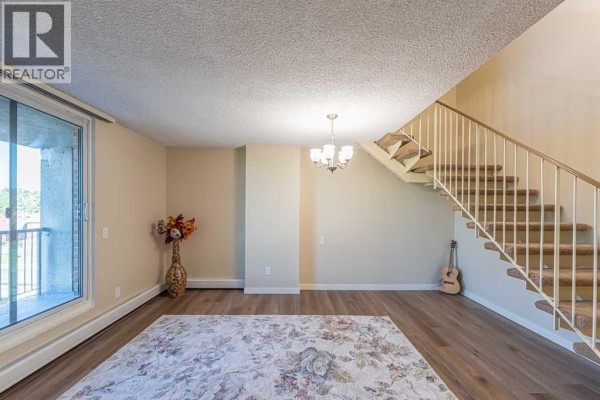A living room with a patterned area rug, staircase, and a guitar leaning against the wall. - 513, 4944 Dalton Drive Nw, Calgary