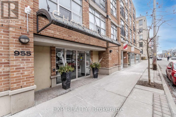 Exterior view of the brick building with glass entrance doors and planters. - 513 - 955 Queen Street W, Toronto