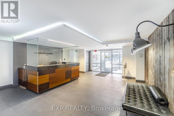 Modern lobby with a reception desk, glass partitions, and a leather bench. - 513 - 955 Queen Street W, Toronto