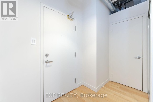 Interior hallway with white doors, light wood floors, and exposed piping overhead. - 513 - 955 Queen Street W, Toronto