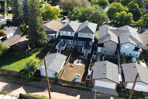 Elevated view of a suburban neighborhood with dense trees and a distant city skyline. - 513 L Avenue N, Saskatoon