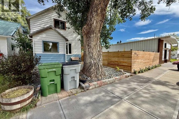 Side view of house with green and grey bins, large tree, and wooden fence. - 5133 50 Street, Provost