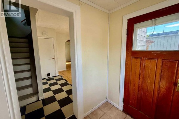 Entryway with dark red door, checkered tile floor, and view of staircase. - 5133 50 Street, Provost