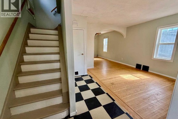 Interior hallway with black and white checkered tile floor, wooden staircase, and archway to living room. - 5133 50 Street, Provost