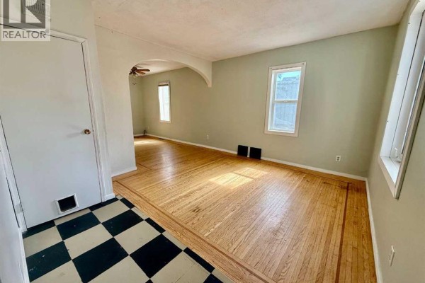 Living room with hardwood floors, light green walls, arched doorway, and windows. - 5133 50 Street, Provost
