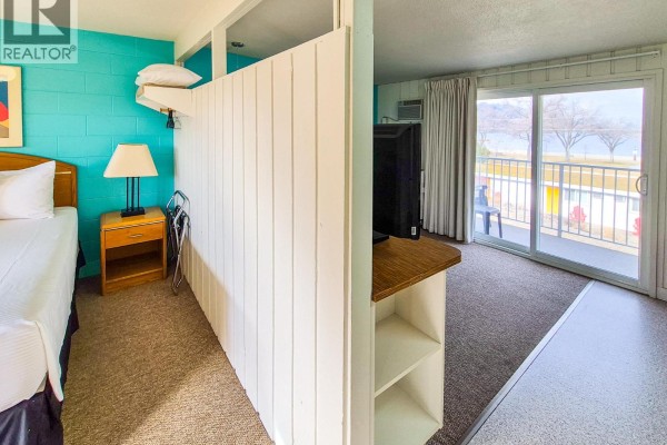 View from the bedroom into the living area and kitchenette, with a balcony door. - 5133 7th Avenue, Okanagan Falls