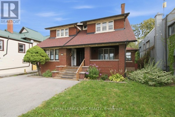 Side view of a red brick house with a porch, green lawn, and driveway. - 5134 Victoria Avenue E, Niagara Falls