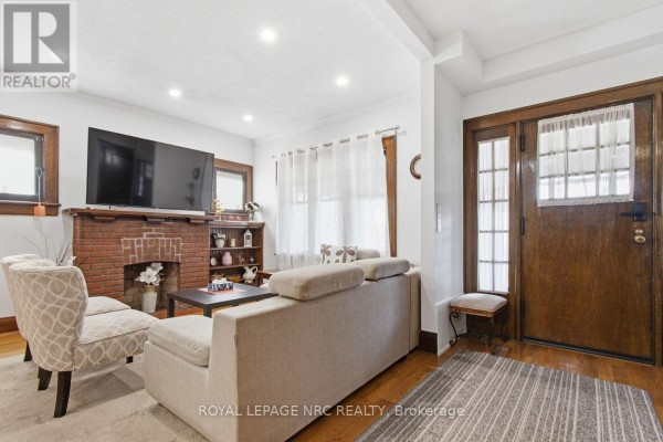 Living room with a brick fireplace, sofa, chairs, and a large television. - 5134 Victoria Avenue E, Niagara Falls