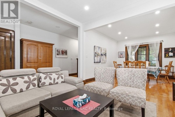 Living and dining area with a sectional sofa, accent chairs, wooden cabinets, and dining set. - 5134 Victoria Avenue E, Niagara Falls