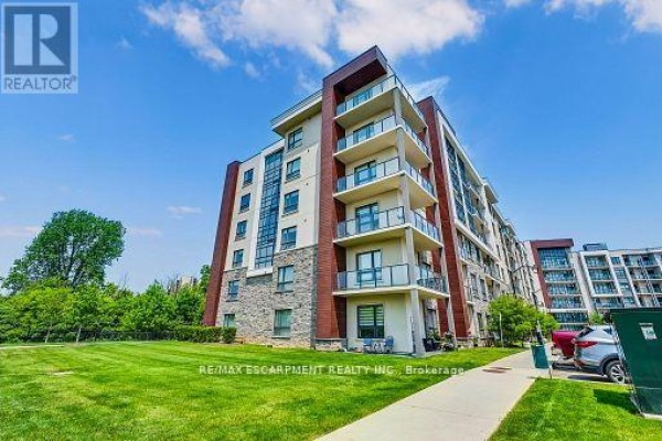 Exterior view of an apartment building with balconies, green lawn, and trees. - 514 - 125 Shoreview Place, Hamilton
